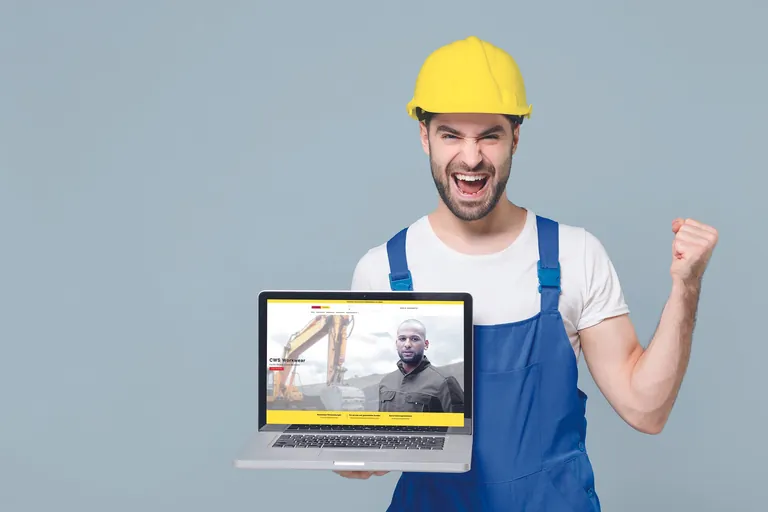 Gl&uuml;cklicher Mann im Overall h&auml;lt aufgeklappten Laptop.