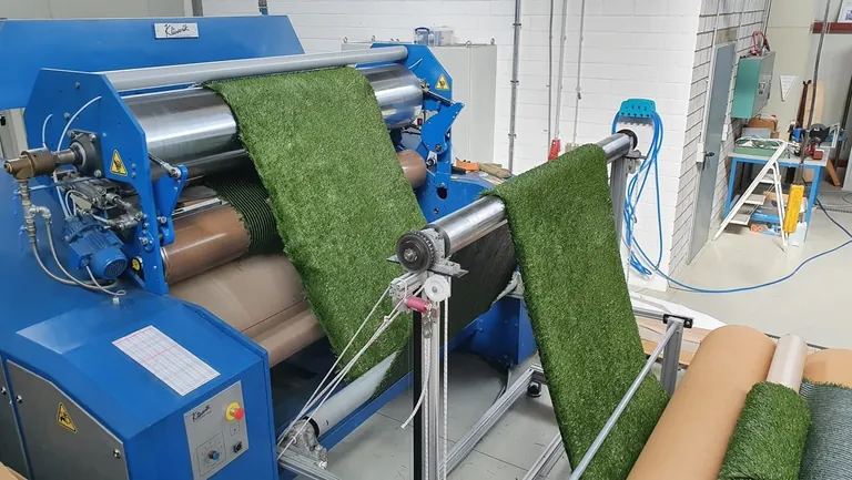 Das Bild zeigt eine Maschine, in der eine Bahn Kunstrasen von BioTurf gespannt ist.