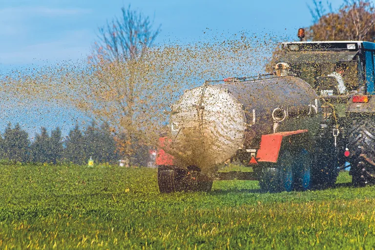 Ein Traktor d&uuml;ngt mit G&uuml;lle ein Feld im Herbst.