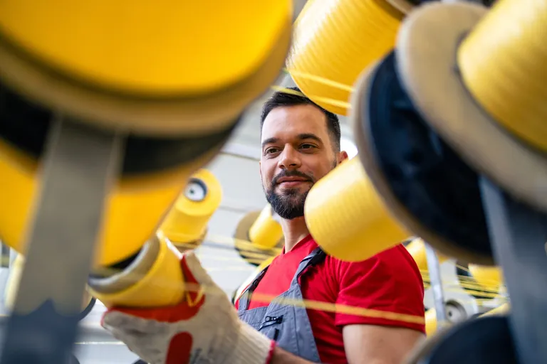 Mann wechselt Garnspule einer industriellen Strickmaschine.