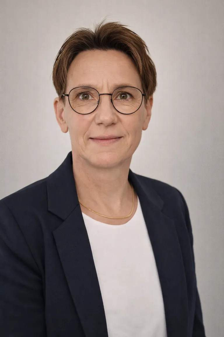 Frau mittleren Alters, kurze braune Haare, runde Brille, Sakko.