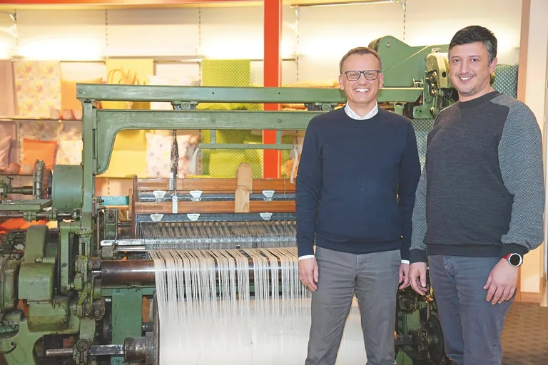 Geschäftsführer Torsten Göth (li.) und CEO Ibrahim Kilicoglu vor einem historischen Webstuhl im Showroom am Standort Külsheim.