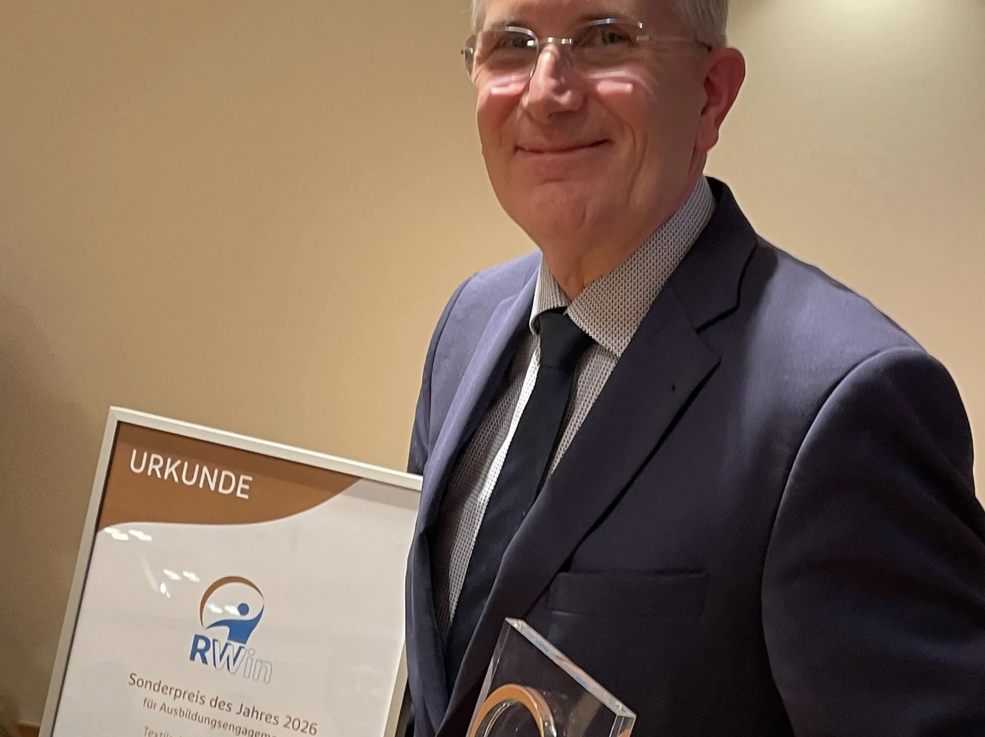 Franz Lang, blauer Anzug und Krawatte, hält die RWin-Urkunde und den RWin-Award in der Hand, lächelt.