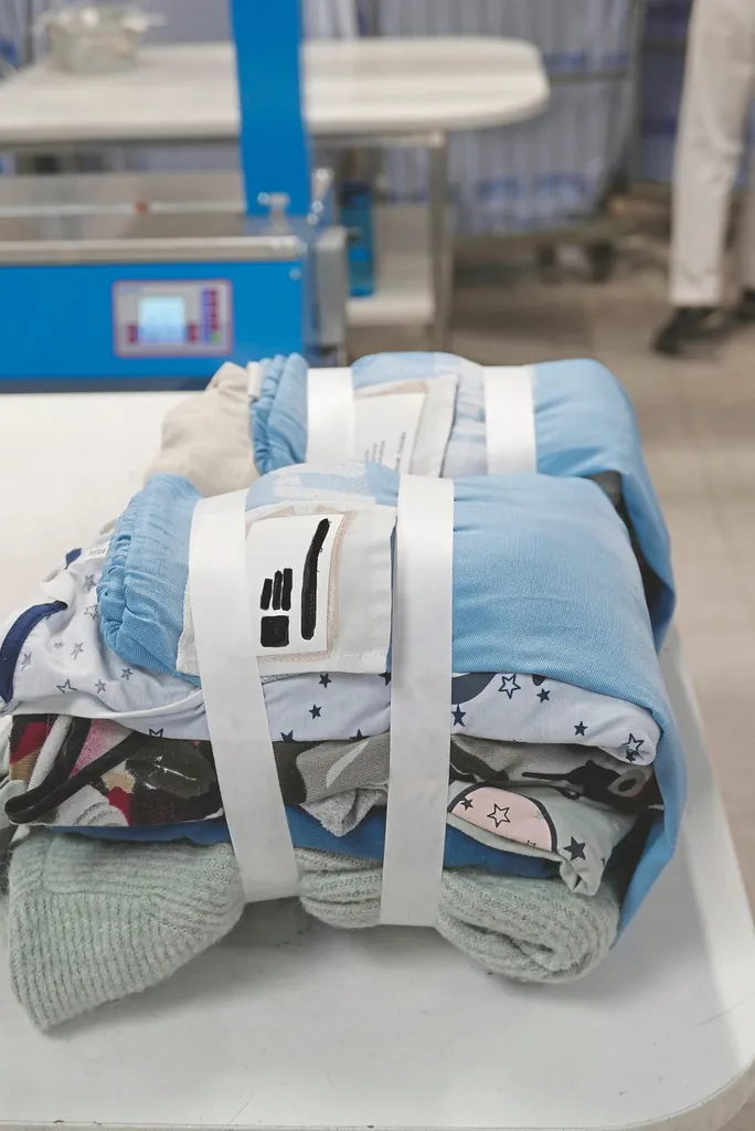 F&uuml;r die Auslieferung der sauberen Bewohnerw&auml;sche wird die Kleidung in einen W&auml;schesack eingeschlagen, mit zwei Papierbanderolen umwickelt und mit einem Label samt Namen des Heims und des Bewohners versehen.