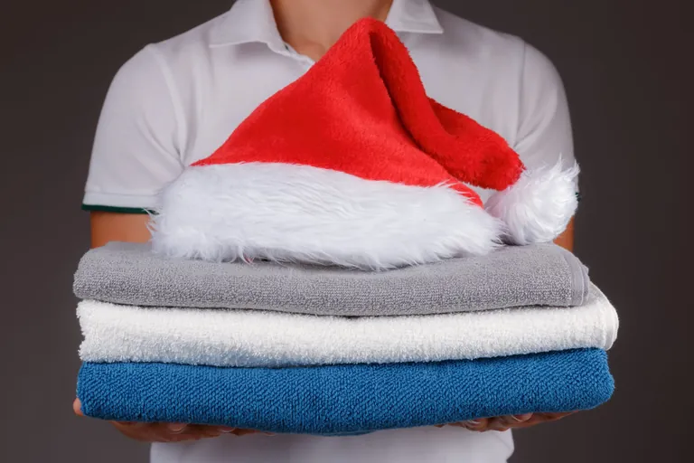Eine Frau hält einen Stapel Handtücher mit einer Weihnachtsmütze, die obendrauf liegt.